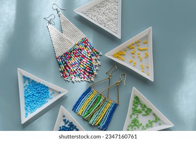 Triangular bead trays with beaded earrings. Different colored seed beads in containers for needlework and beading. Creativity and  hobby concept