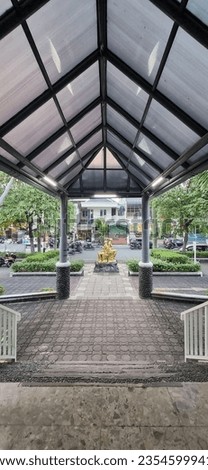 A triangular canopy made of polycarbonate is in front of the entrance for drop off, in the middle of which there is a golden statue of a seated woman as a decoration.