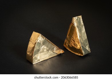 Triangular cream cheeses wrapped in foil on a black background. Portioned triangular cheeses.