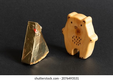 Triangular cream cheeses wrapped in foil next to a wooden toy in the shape of a bear on a black background. Portioned triangular cheeses. Food for children - Shutterstock ID 2076493531