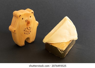 Triangular cream cheeses wrapped in golden aluminium foil and without packaging next to a wooden toy in the shape of a bear on a black background. Portioned triangular cheeses. Food for children - Shutterstock ID 2076493525