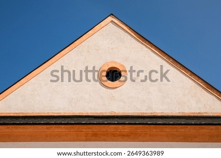 Triangular gable with round window showing blue sky in Czech Republic