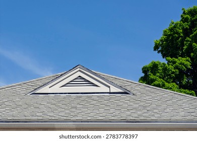Triangular gable vent on an asphalt shingle roof under a bright blue sky