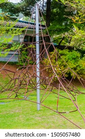 Triangular Iron Rope Jungle Gym In Manicured Lawn With Trees And Building In Background.