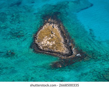 A triangular islet with sparse vegetation and rocky formations surrounded by clear turquoise waters near Elafonisi beach on the island of Crete.