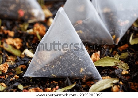 Triangular pyramidal tea bags filled with flavored black tea, with fruits, berries and flowers, lie next to a pile of flavored black tea. Macro. Selective focus. Close-up