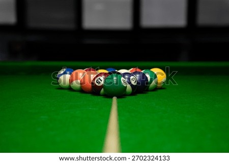 Triangular rock of colorful pool balls on a bright green felt table, with a wooden cue stick pointed towards the break.