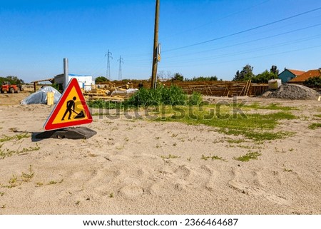 Triangular traffic sign with caution symbol of warning, work in progress, placed in front of construction site zone area.