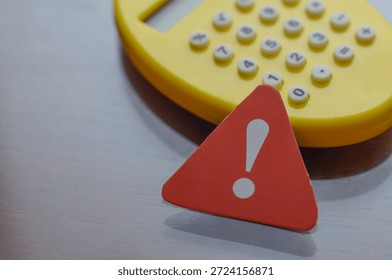 Triangular warning sign in foreground with blurred calculator behind, representing calculation error or financial caution. - Powered by Shutterstock - Get 15% off with code: PIKWIZARD15