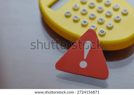 Triangular warning sign in foreground with blurred calculator behind, representing calculation error or financial caution.