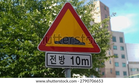 A triangular yellow and red speed bump warning traffic sign with an additional rectangular plate indicating ten meters ahead.