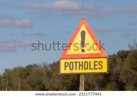 Triangular yellow road traffic warning sign for Potholes at the side of a rural road