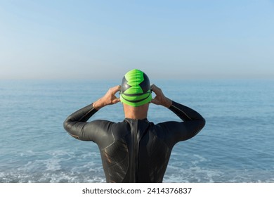 Triathlete preparing to swim- putting on swimming cap and goggles- rear view - Powered by Shutterstock