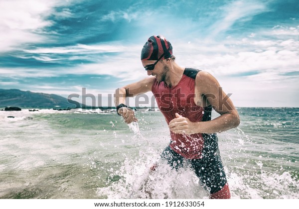 Triathlete swimmer looking at sport watch app\
using smartwatch during triathlon. Swimming man running out of\
ocean swim checking heart rate on smart watch. Professional athlete\
training for\
ironman.