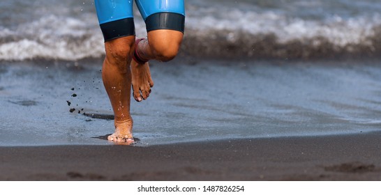 Triathlete Swimmer Running Out Of Ocean Finishing Swim Race.Fit Man Ending Swimming Sprinting Determined Out Of Water In Professional Triathlon Suit For Ironman