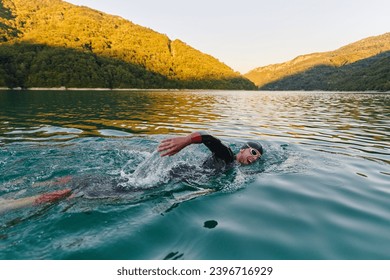 Triathlon athlete swimming on lake in sunrise wearing wetsuit - Powered by Shutterstock