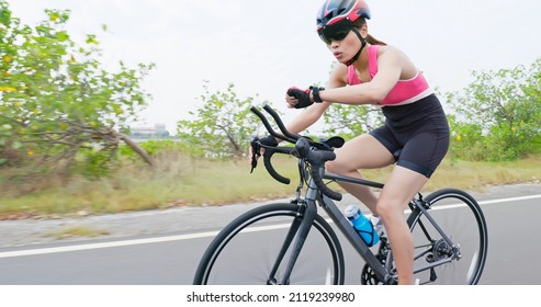 Triathlon bike training - asian young woman wearing helmet is riding a bicycle and Checking Her Fitness Stats on Smart Watch on the road concentratedly - Powered by Shutterstock