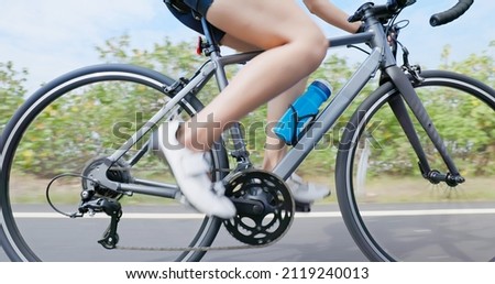 Triathlon bike training - close up legs of asian young woman is riding a bicycle with water bottle on the road concentratedly