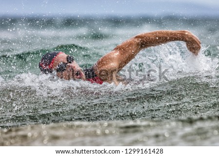 Triathlon swim tired swimmer swimming in ocean in wave and rain storm . Professional male triathlon swimmer wearing cap, goggles and red triathlon tri suit training for ironman breathing out of water. ストックフォト © 