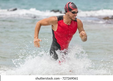 Triathlon swimming man. Male triathlete swimmer running out of ocean finishing swim race. Fit man ending swimming sprinting determined out of water in professional triathlon suit training for ironman. - Powered by Shutterstock