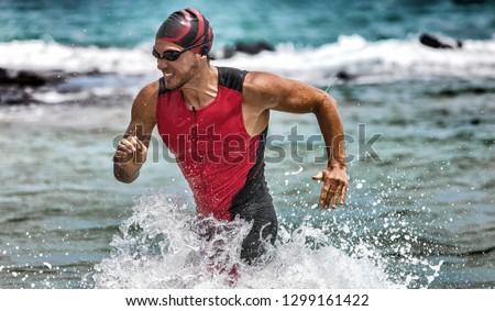 Triathlon swimming man running out of water during ironman race. Male triathlete finishing swim time competition. Fit athlete swimmer sprinting determined out of water in professional tri suit. ストックフォト © 