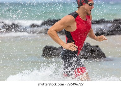 Triathlon Swimming Man Triathlete Swimmer Running Out Of Ocean Finishing Swim Competition. Fit Male Athlete Ending Swimming Sprinting Out Of Ocean With Water Splashing Background Training For Ironman.