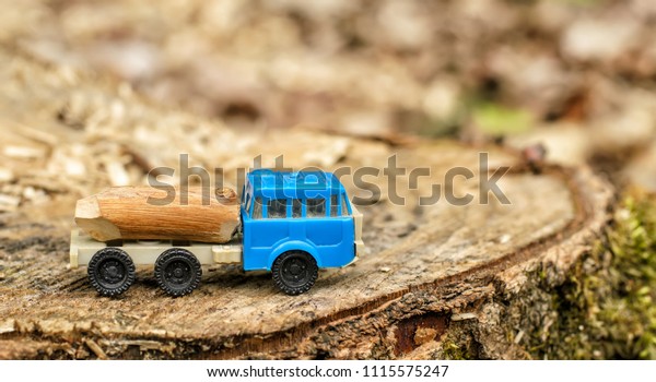 Triaxial toy truck\
with blue cabin, loaded with wood and located on a tree stump,\
blurred background, free space on the right, deforestation and\
environmental protection\
theme