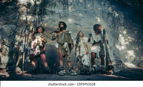Tribe of Four Hunter-Gatherers in Animal Skin Holding Stone Tipped Tools, Pose at Entrance of their Cave. Portrait of Neanderthal Family and their Way of Living. The Shot is Done with Cold Filter