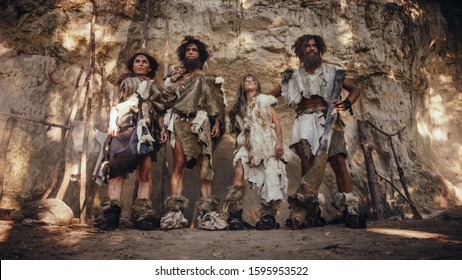 Tribe of Four Hunter-Gatherers Wearing Animal Skin Holding Stone Tipped Tools, Pose at the Entrance of their Cave. Portrait of Two Grown Male and Two Female Neanderthals and their Way of Living