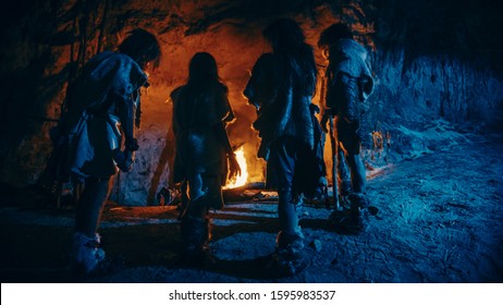 Tribe of Prehistoric Hunter-Gatherers Wearing Animal Skins Live in a Cave at Night. Neanderthal or Homo Sapiens Family Trying to Get Warm at the Bonfire, Holding Hands over Fire. Back View