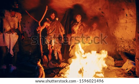 Tribe of Prehistoric Hunter-Gatherers Wearing Animal Skins Stand Around Bonfire Outside of Cave at Night. Portrait of Neanderthal / Homo Sapiens Family Doing Pagan Religion Ritual Near Fire
