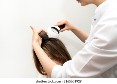 A trichologist examines the condition of the hair on the patient’s head with a dermatoscope. In a bright cosmetology room.