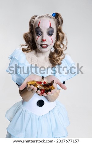 Trick or treat. Close-up mystical blonde girl in Halloween make up and spooky facial expression eating jelly sweets isolated over grey background. Concept of costume party, fashion, creativity, ad