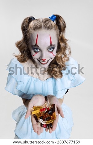 Trick or treat. Close-up mystical blonde girl in Halloween make up and spooky facial expression eating jelly sweets isolated over grey background. Concept of costume party, fashion, creativity, ad