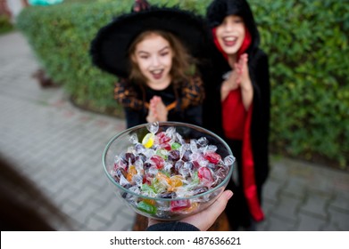 Trick oder Treat. Zwei Kinder, Junge und Mädchen, in schwarzen Anzügen zu Halloween nehmen Bonbons. Im Vordergrund eine Hand mit der Vase gefüllt mit Süßigkeiten. Eva of All Saints' Day.