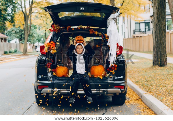 Trick\
or trunk. Child boy celebrating Halloween in trunk of car. Kid with\
red carved pumpkin celebrating traditional October holiday outdoor.\
Social distance and safe alternative\
celebration.