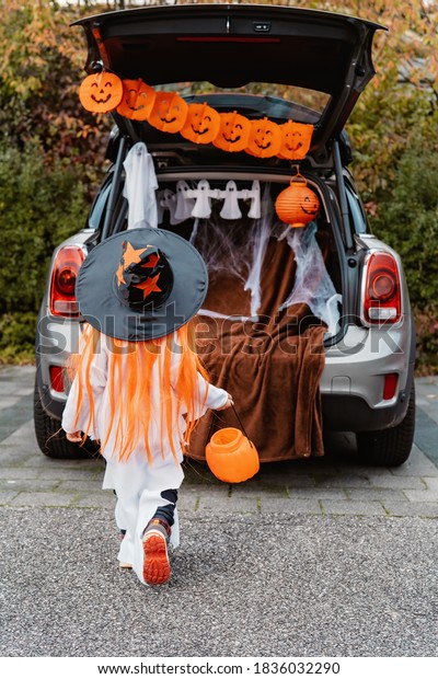 Trick or\
trunk. Trunk or treat. Little child in Halloween witch hat walk to\
decorated trunk of car for candies. New trend and alternative safe\
outdoor celebration of traditional\
holiday.