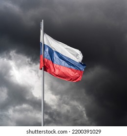 The Tricolor Flag Of Russia White Blue Red On A Flagpole Against The Background Of Dark Storm Clouds As A War Close-up