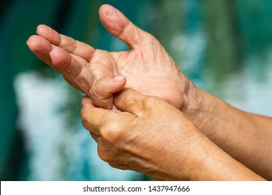 Trigger Finger, Senior woman's left hand massaging her little finger, Suffering from pain, Close up & macro shot, Swimming pool background, Office syndrome, Healthcare and massage asian body concept