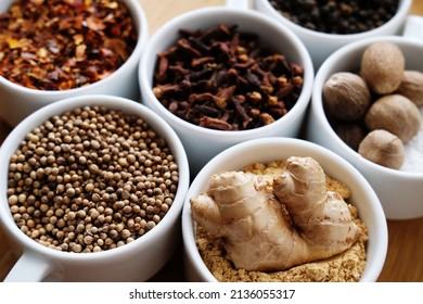 Trikatu plus spices and herbs: ginger, nutmeg, coriander, cayenne pepper, cloves and black pepper. Ayurvedic traditional herbal remedy. Whole ingredients in white cups on wooden background - Shutterstock ID 2136055317