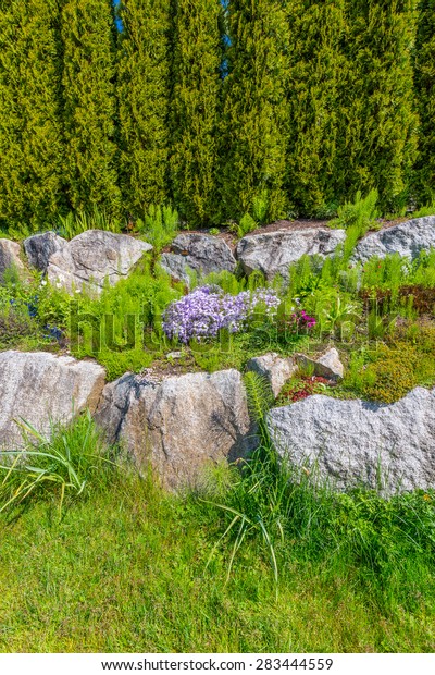 Trimmed bushes, flowers and\
stones in nicely decorated front yard, lawn of the house. Landscape\
design.