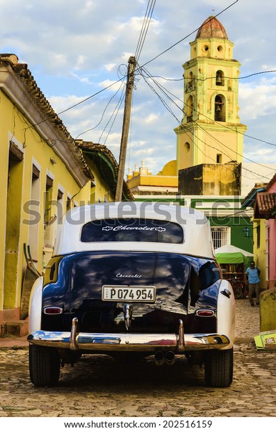 TRINIDAD, CUBA - DECEMBER 8, 2013: Black and white\
classic American car and colorful colonial building in streets of\
Trinidad, where old cars are relic of Cuban revolution and attracts\
many tourists. 