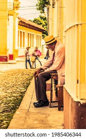 Trinidad, Cuba - July 15 2018 :A Former Spanish Colonial Town Still In The 18th Century With A Older Man In Business Cloths With Hat On Sitting Outside On The Side Walk On A Chair 