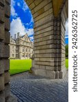 Trinity College Dublin, Ireland. The image features a view of the college through a stone archway, with cobblestones and trees in the foreground. The college