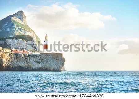 Trinity lighthouse at the rocky shore (cliffs) of the Europa Point. British Overseas Territory of Gibraltar, Mediterranean sea. Epic cloudscape. National landmark, sightseeing, travel destination