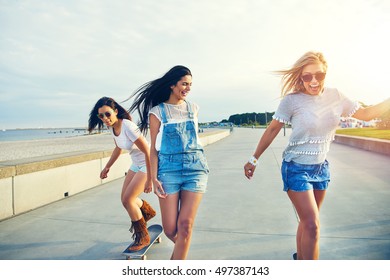 Trio of attractive carefree young women enjoying an early morning at the seaside laughing as they skateboard along a beachfront promenade - Powered by Shutterstock