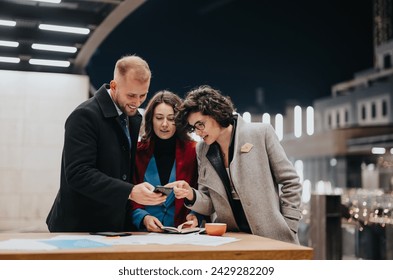 A trio of business colleagues intimately engaged in discussing digital content on a smart phone, with a night-time city backdrop. - Powered by Shutterstock