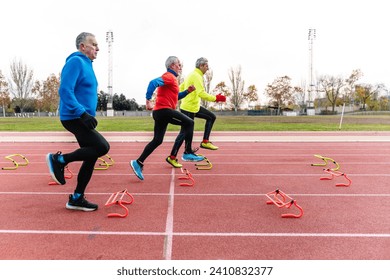 A trio of elderly men engaging in agility training with colorful hurdles on an athletic track - Powered by Shutterstock