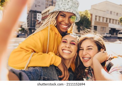 Trio of friends taking a selfie together. Group of multiethnic female friends having fun together outdoors. Cheerful generation z friends capturing their happy moments in the city. - Shutterstock ID 2111152694