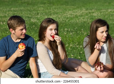 Trio Of Happy Caucasian Teenagers Eating Fruit Outdoors